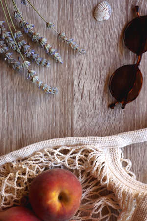 Sunglasses, vintage books, reusable mesh bag with fresh peaches, seashell and lavender flowers on wooden background Boho and rustic summery details, flat lay.の写真素材