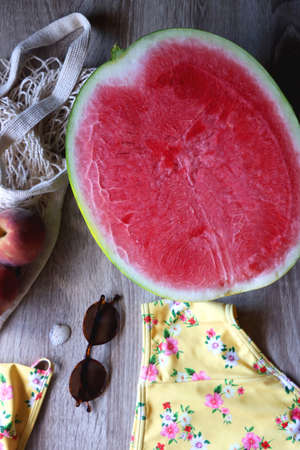 Yellow floral swimming suit, sunglasses, mesh tote with fresh peaches, seashell, watermelon half and...