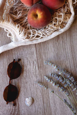 Sunglasses, vintage books, reusable mesh bag with fresh peaches, seashell and lavender flowers on...