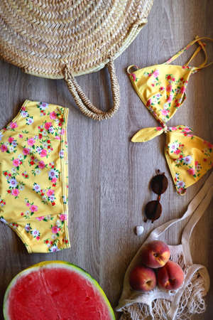 Yellow floral swimming suit, sunglasses, mesh tote with fresh peaches, seashell, watermelon half and...
