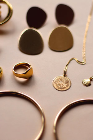 Various gold jewelry and pearl hair clips on peach colored background. Selective focus.