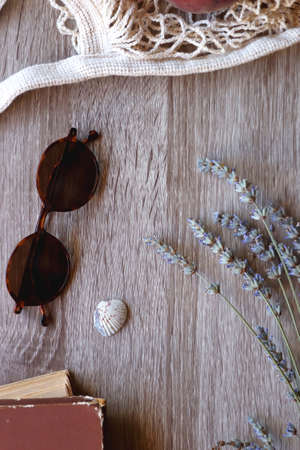 Sunglasses, vintage books, reusable mesh bag with fresh peaches, seashell and lavender flowers on wooden background Boho and rustic summery details, flat lay.の写真素材