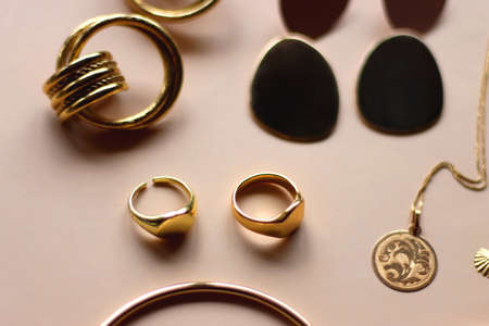 Various gold jewelry and pearl hair clips on peach colored background. Selective focus.の写真素材