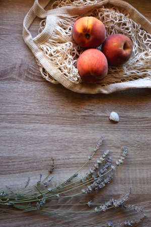 Sunglasses, vintage books, reusable mesh bag with fresh peaches, seashell and lavender flowers on wooden background Boho and rustic summery details, flat lay.の写真素材