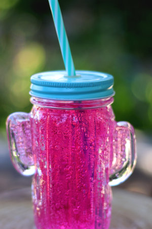 Cactus shaped glass filled with pink soda in the garden. Refreshing summer drink. Selective focus.の写真素材