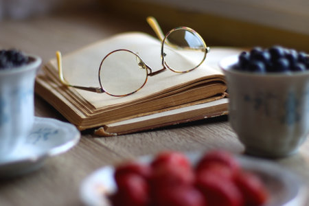 Vintage tea set filled with blueberries, blackberries and starwberries, open book, reading glasses...