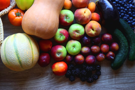 Round straw bag and various healthy fruits and vegetables on wooden background. Top view.
