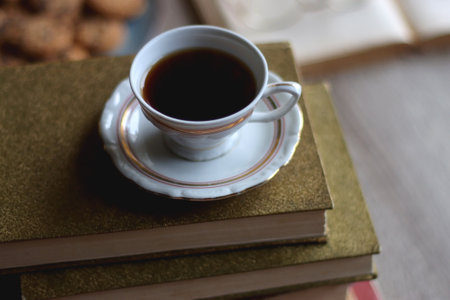 Plate of chocolate chip cookies, stack of vintage books, reading glasses, cup of tea or coffee, lit...