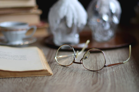 Stack of vintage books, cup of tea or coffee, lit candles, reading glasses and chess pieces on...