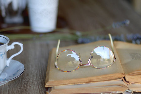 Cup of tea, plate with chocolate chip cookies, open book, reading glasses, lit candles and dry lavender flowers. Hygge at home, selective focus.の写真素材