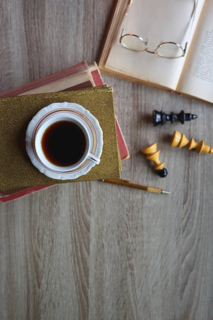 Cup of tea or coffee, stack of old books, reading glasses, pen and chess pieces on wooden table. dark academia concept. Top view.の写真素材