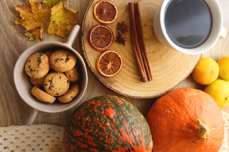 Cup of tea or coffee, seasonal spices, bowl of cookies, blanket, pumpkins, colorful leaves, books and tangerines on wooden table. Cozy hygge at home. Top view.の写真素材