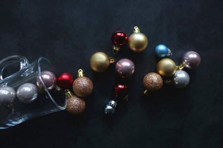 Glass with colorful Christmas baubles on dark background. Top view.