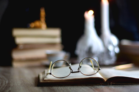 Stack of vintage books, cup of tea or coffee, lit candles, reading glasses and chess pieces on...