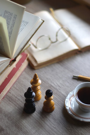 Stack of vintage books, cup of tea or coffee, lit candles, reading glasses and chess pieces on wooden table. Dark academia concept. Selective focus.の写真素材