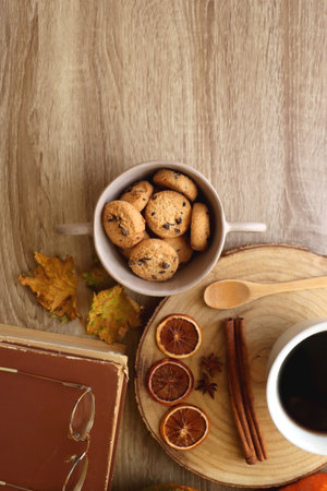 Cup of tea or coffee, seasonal spices, bowl of cookies, blanket, pumpkins, colorful leaves, books and tangerines on wooden table. Cozy hygge at home. Top view.の写真素材