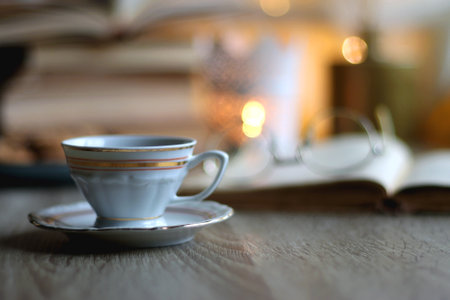 Plate of chocolate chip cookies, stack of vintage books, reading glasses, cup of tea or coffee, lit...