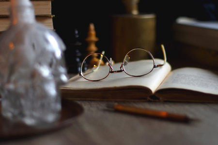 Stack of vintage books, cup of tea or coffee, lit candles, reading glasses and chess pieces on wooden table. Dark academia concept. Selective focus.の写真素材