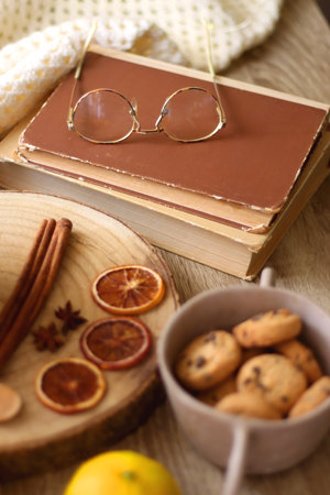 Cup of tea or coffee, various spices, bowl of cookies, tangerines, books, reading glasses and knitted blanket on wooden table. Hygge at home concept, selective focus.の写真素材
