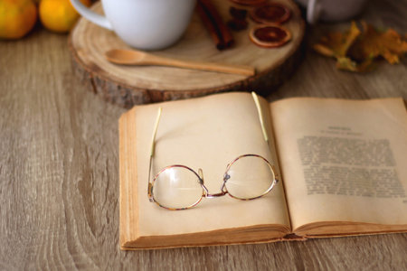 Cup of tea or coffee, seasonal spices, bowl of cookies, blanket, pumpkins, colorful leaves, books and tangerines on wooden table. Cozy hygge at home. Selective focus.の写真素材