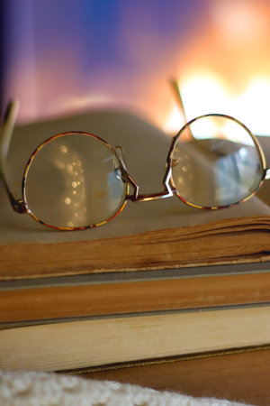 Stack of books, soft blanket, books and reading glasses on the table in front of a fireplace. Selective focus.の写真素材