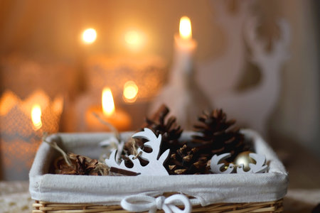 Basket with pine cones, Christmas ornaments and seasonal spices. Soft blanket, and lit candles in...