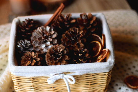 Basket with pine cones and seasonal spices on the table. Lit candles in the background. Hygge at home. Selective focus.の写真素材