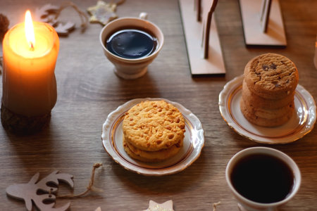 Two types of cookies, cups of tea or coffee, various Christmas decorations and lit candles. Cozy Christmas atmosphere at home. Selective focus.の写真素材