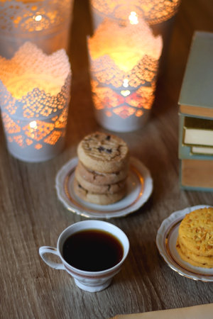 Plates with various cookies, cups of tea or coffee, vintage books, reading glasses and lit candles on the table. Selective focus.の写真素材