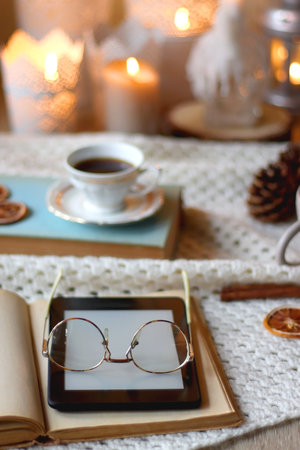 Cup of tea, books, tablet, bowl of cookies, various spices, pine cones and lit candles. Hygge at home. Selective focus.の写真素材