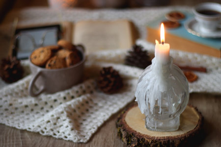 Cup of tea, books, tablet, bowl of cookies, various spices, pine cones and lit candles. Hygge at home. Selective focus.の写真素材