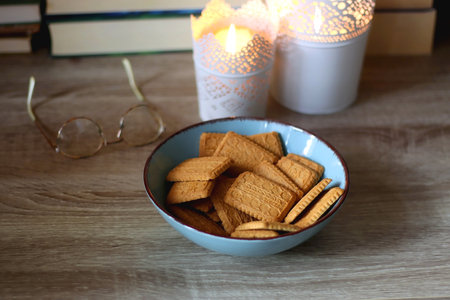 Glasses, bowl of biscuits, lit candles and books in the background. Selective focus.