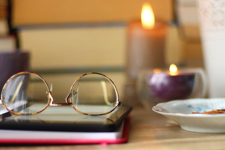 Notebook, pen, tablet, reading glasses, books, phone, candle, bowl of biscuits and cup of tea on the table. Selective focus.の写真素材