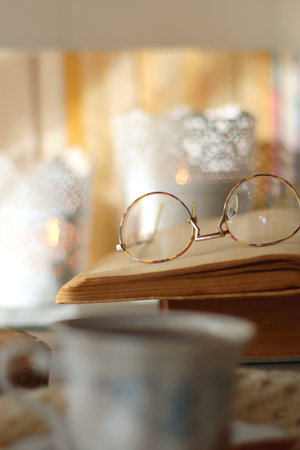 Vintage books, reading glasses, e-reader, cup of tea, bowl of biscuits and lit candle on the table....