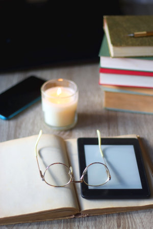 Pile of books, tablet, reading glasses, mobile phone, scented candle, pen and laptop on the table. Selective focus.の写真素材