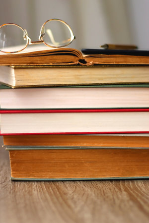Pile of books, tablet, reading glasses and pen on the table. Selective focus.