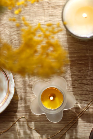 Retro bag, plate with gold rings and earrings, gold necklace, sunglasses, face roller, lit candles and mimosa flowers on wooden background. Flat lay.の写真素材