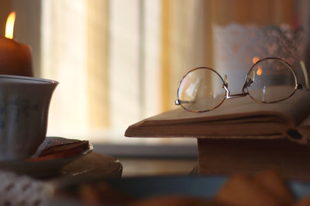 Vintage books, reading glasses, e-reader, cup of tea, bowl of biscuits and lit candle on the table. Selective focus.の写真素材