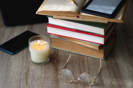 Pile of books, tablet, reading glasses, mobile phone, scented candle, pen and laptop on the table. Selective focus.の写真素材