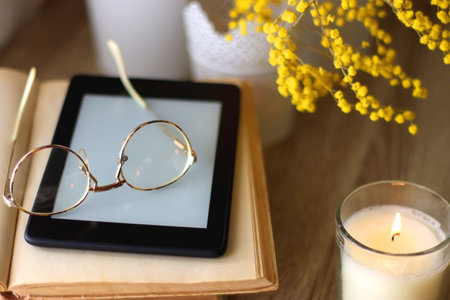 Scented candles, chocolate, cookies, cup of tea, books, e-reader, glasses and flowers on the table. Hygge at home. Selective focus.の写真素材