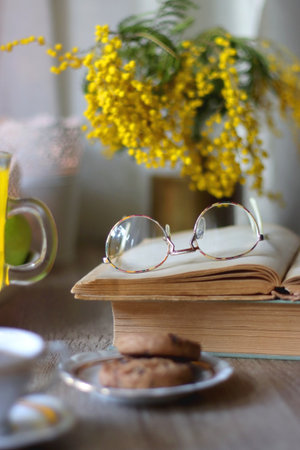 Cup of tea, plates with cookies, glass of orange juice, books, reading glasses, bowl of fruit and candles on the table. Selective focus.の写真素材