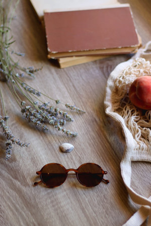 Mesh tote with fresh peacehs, lavender bouquet, round sunglasses, vintage book and seashell on the table. Selective focus.の写真素材