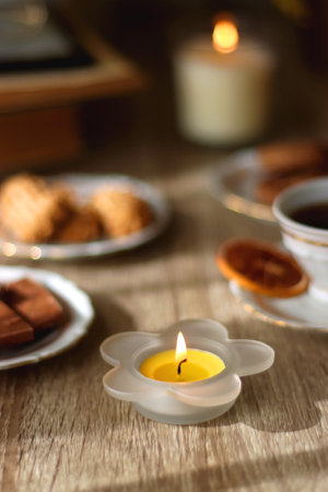 Scented candles, chocolate, cookies, cup of tea, books, e-reader, glasses and flowers on the table. Hygge at home. Selective focus.の写真素材