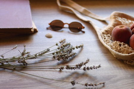Mesh tote with fresh peacehs, lavender bouquet, round sunglasses, vintage book and seashell on the...