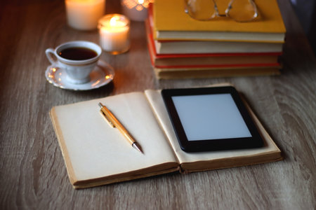 Cup of tea or coffee, plate of cookies, books, e-reader, pencil and lit candles on the table. Selective focus.の写真素材