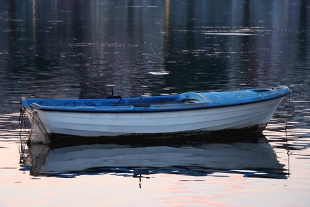 Small boat moored in shallow sea. Soft sunset light reflects in the sea. Selective focus.