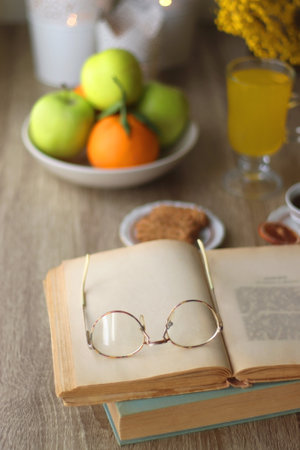 Cup of tea, plates with cookies, glass of orange juice, books, reading glasses, bowl of fruit and candles on the table. Selective focus.の写真素材