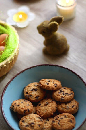 Easter eggs in the basket, bowl of cookies, chocolate pralines, Easter bunny figurine, cups of tea,...