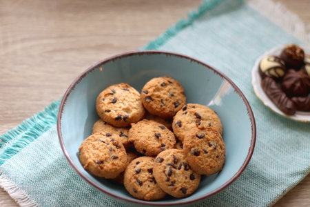 Plate of chocolate pralines, bowl of cookies, cups of tea, glasses of juice and lit candles on the table. Selective focus.の写真素材