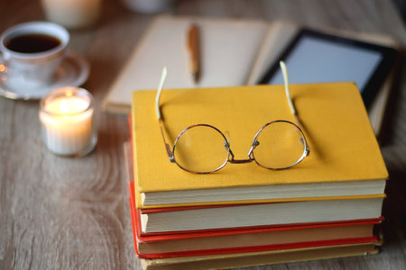 Cup of tea or coffee, plate of cookies, books, e-reader, pencil and lit candles on the table....